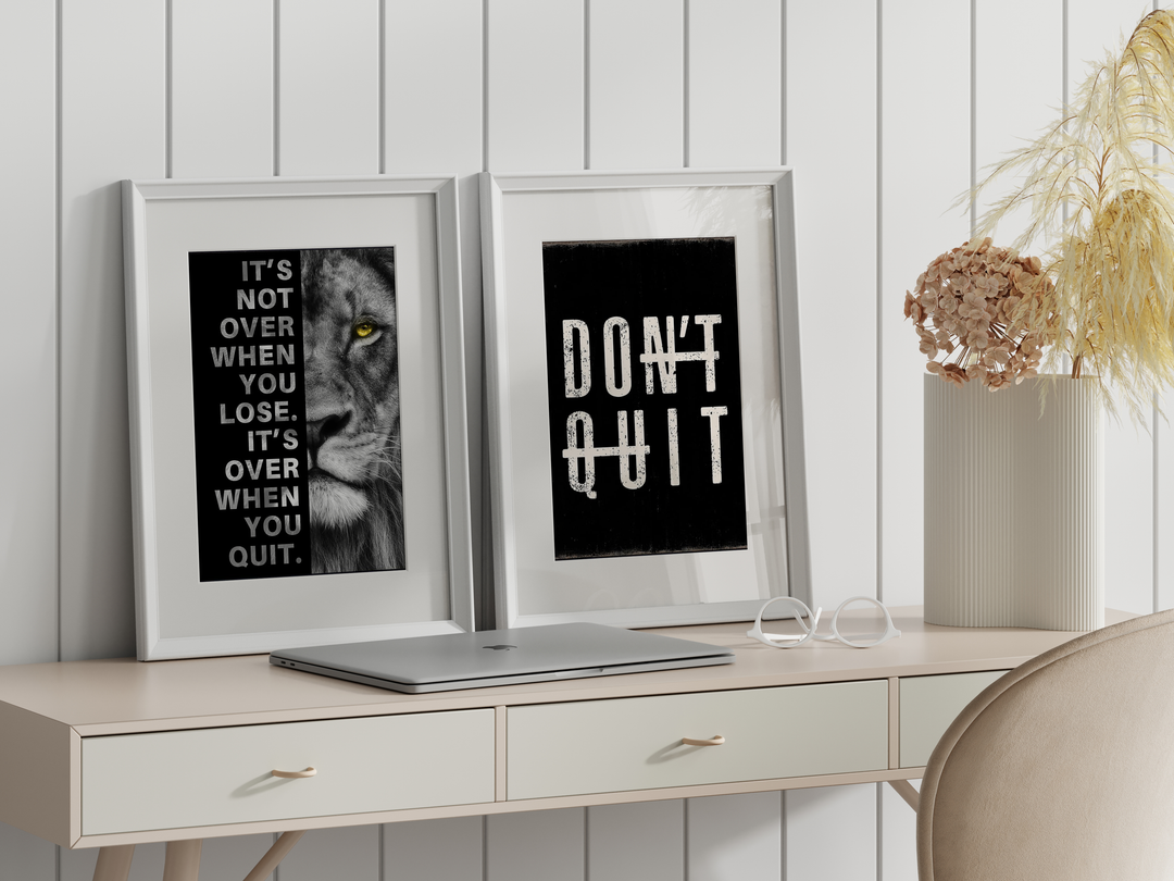 Motivational wall art prints in white frames on a desk with a plant